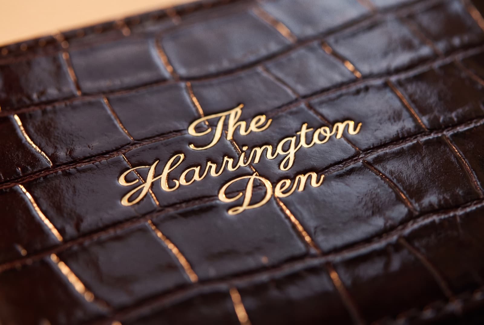 The Harrington Den pressed in gold script, close enough to see the foil edges in the grain
