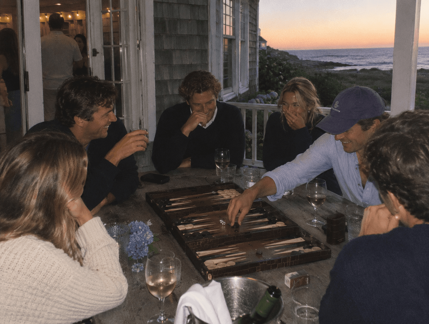 Friends playing backgammon on a coastal porch at dusk